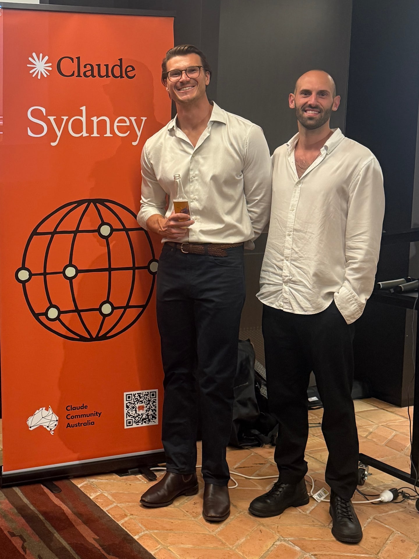 Miguel Pieters and Thibault Calliauw of Onwise standing beside the orange Claude Sydney banner from Claude Community Australia